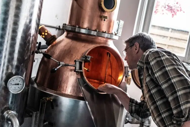 Ein Mann inspiziert das Innere eines großen kupfernen Destillationstanks.