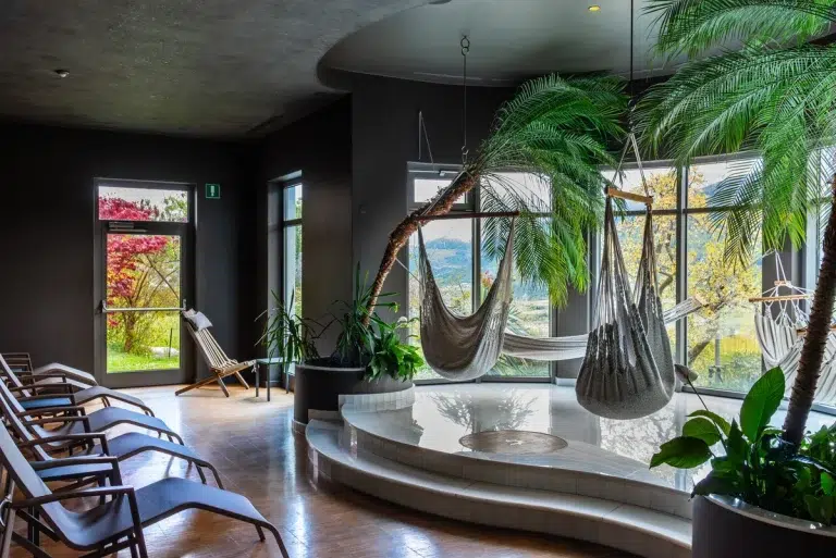 Moderne Indoor-Lounge mit Hängematten, Liegestühlen, großen Fenstern und üppigen Grünpflanzen.