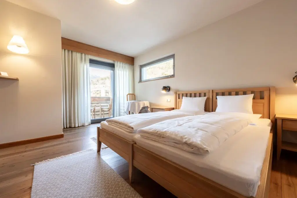 Helles Hotelzimmer mit zwei Einzelbetten, Holzboden, Balkon und hellem Dekor.