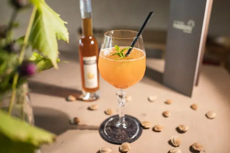 Ein pfirsichfarbener Cocktail im Biohotel Südtirol, mit Minze und Nüssen garniert.