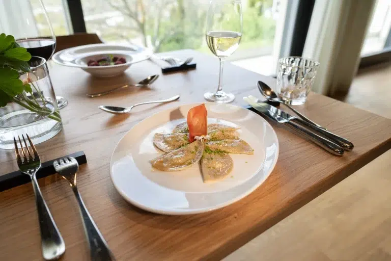 Ein Teller Ravioli mit Beilage, serviert an einem gedeckten Tisch mit Wein und Wasser.