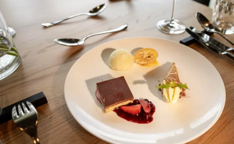Ein Dessert-Trio mit Kuchen, Eis und Obst auf einem weißen Teller auf einem Holztisch.