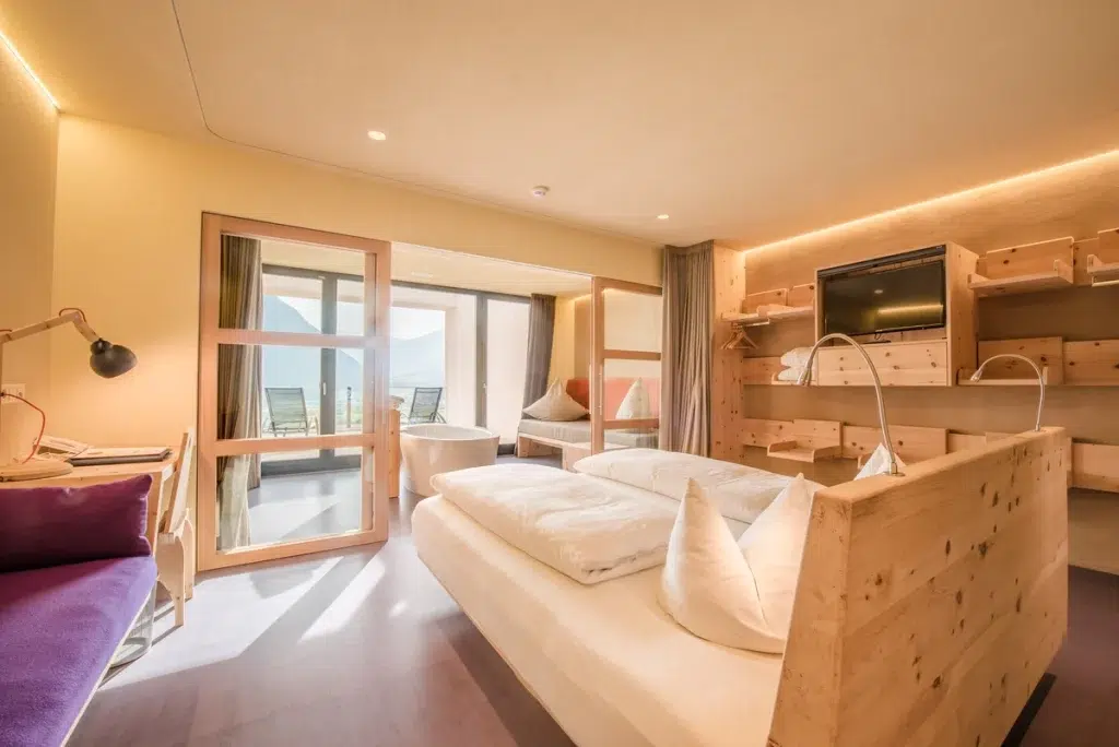 Helles Hotelzimmer mit Holzmöbeln, Doppelbett, Balkon und Bergblick.