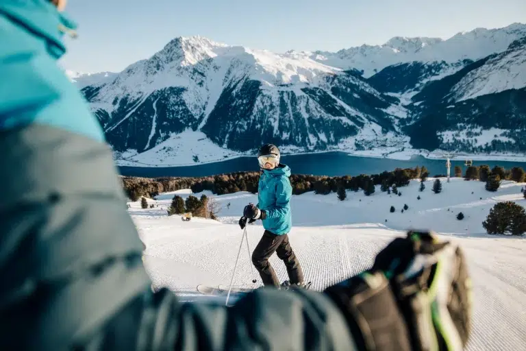 Zwei Personen beim Skifahren an einem See mit schneebedeckten Gipfeln, in der Nähe des Biohotels Südtirol.