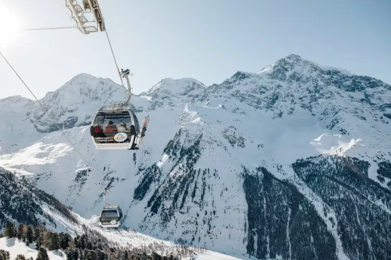 An einem klaren, sonnigen Tag fahren zwei Skigondeln über eine verschneite Berglandschaft.