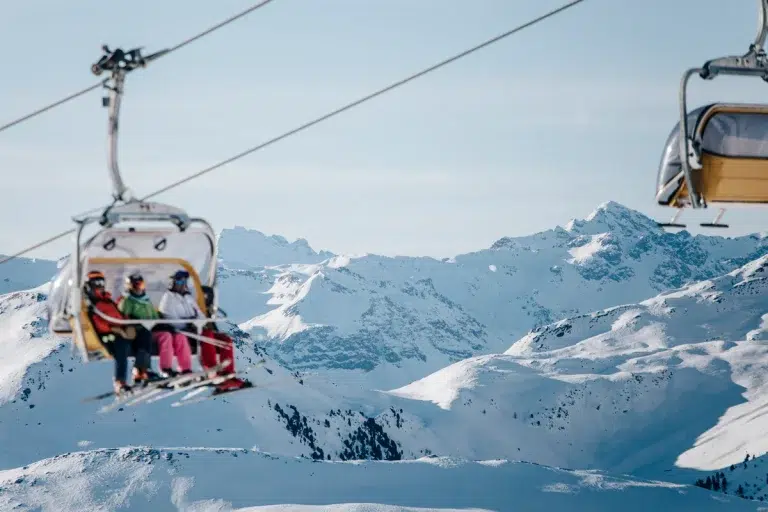 Menschen auf einer Skiliftfahrt über verschneite Berge unter einem klaren blauen Himmel.