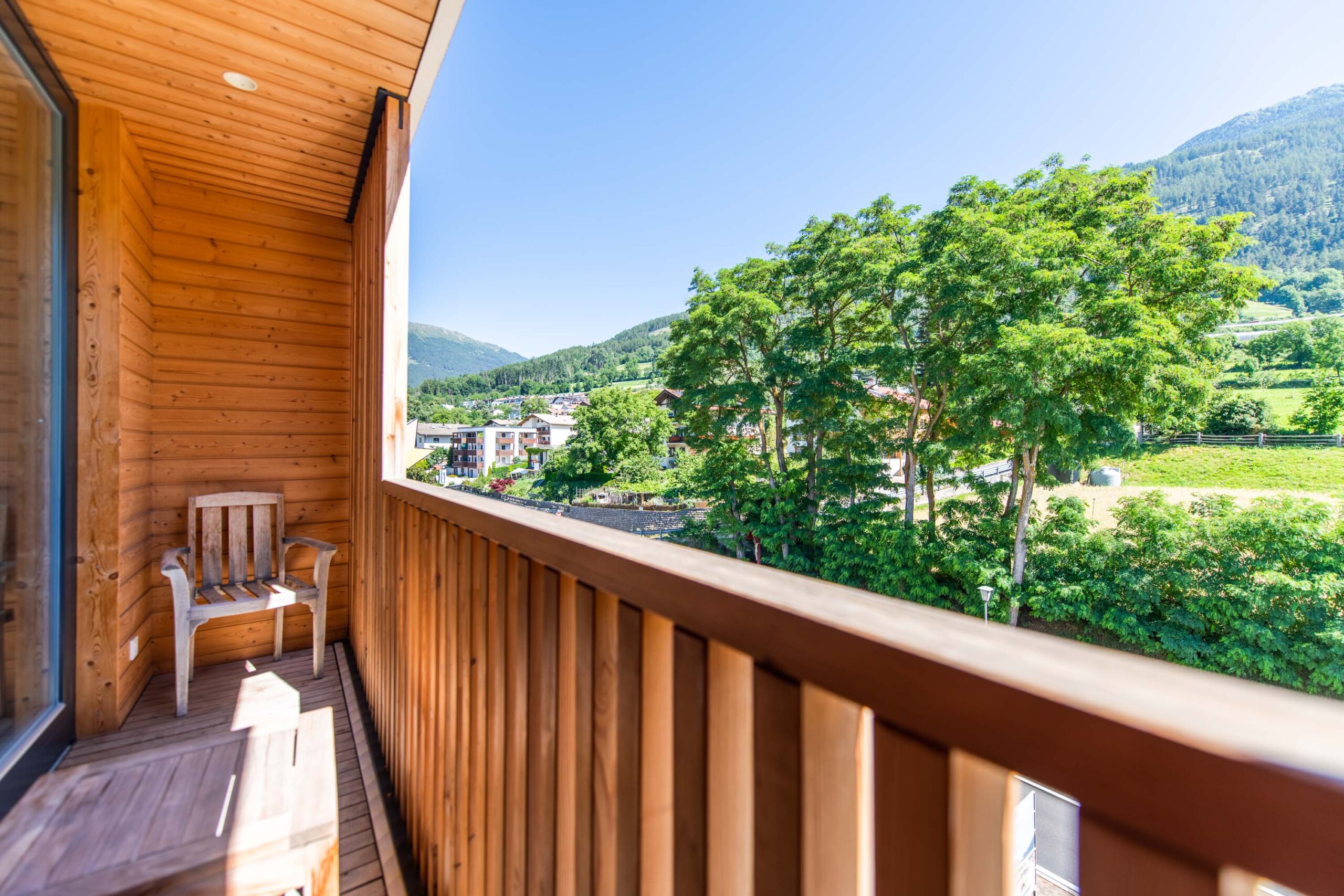 Holzbalkon des Biohotels Südtirol mit Stuhl und Blick auf Bäume und ferne Hügel.