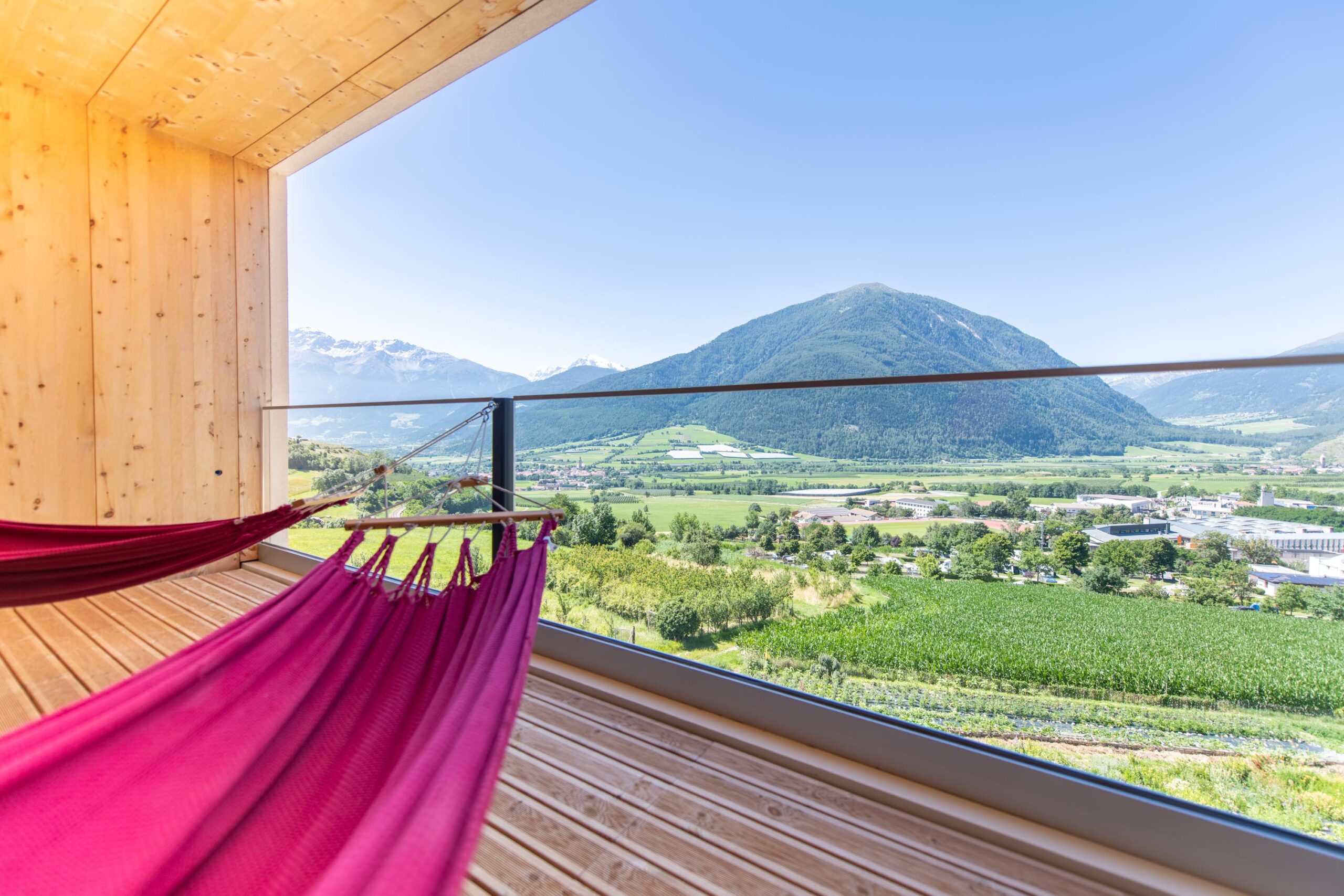 Rosa Hängematte auf einem Holzbalkon im Biohotel Südtirol mit Blick auf grüne Berge und das Tal.