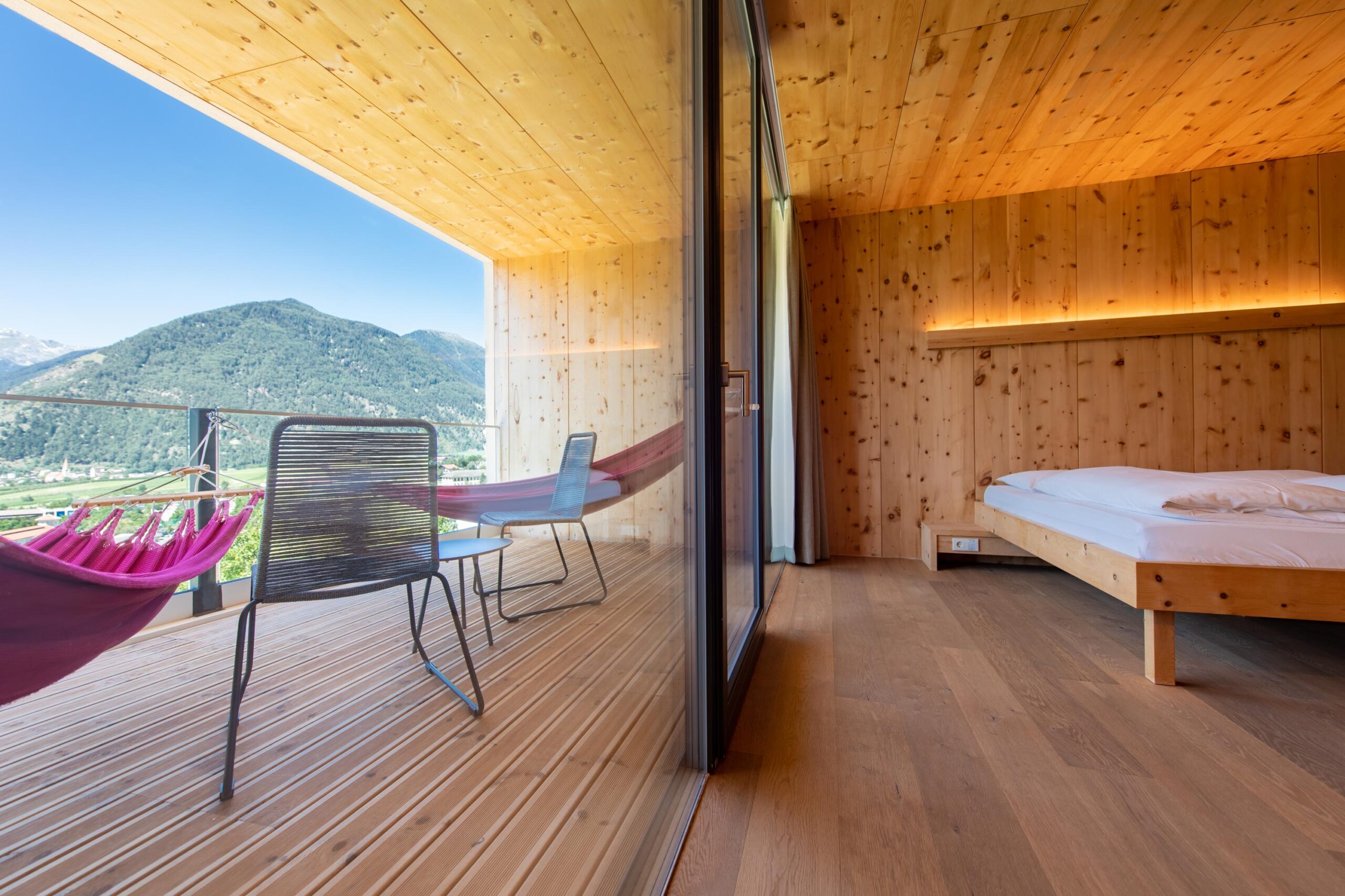 Modernes Holzzimmer im Biohotel Südtirol mit Hängemattenbalkon und Blick auf die grünen Berge.