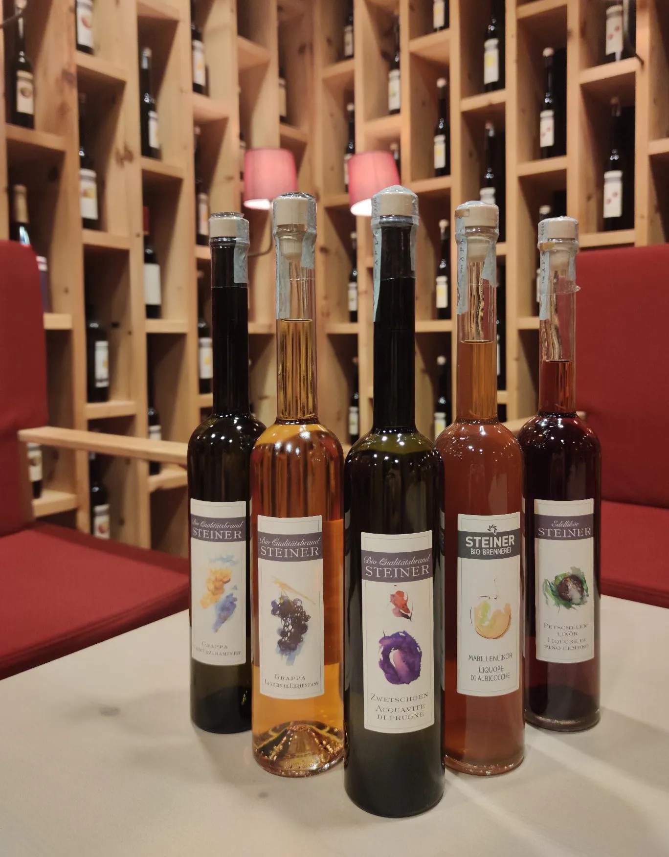 Fünf Flaschen Bio Brennerei Steiner Likör auf einem Tisch in einer Weinhandlung mit Holzregalen.
