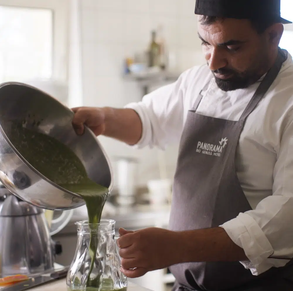 Ein Koch gießt in einer Küche grüne Bio-Eigenproduktion aus einer Schüssel in ein Glasgefäß.