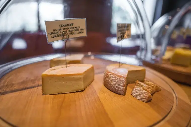 Genießen Sie ein Frühstückspanorama: zwei Käsesorten auf einem Holzbrett, jede unter einer Glaskuppel beschriftet.