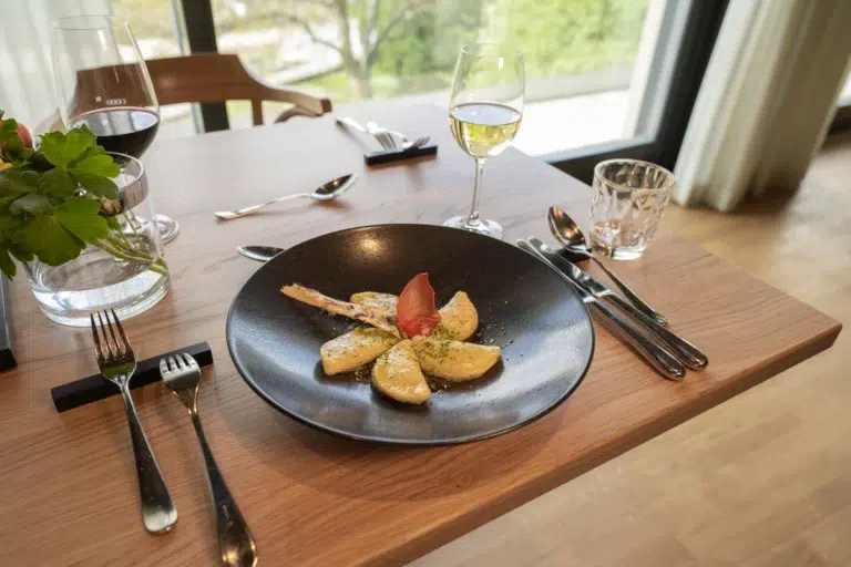 Ein schwarzer Teller mit Kartoffelscheiben, Hoteldiät-Garnitur und Weißwein auf einem Holztisch.