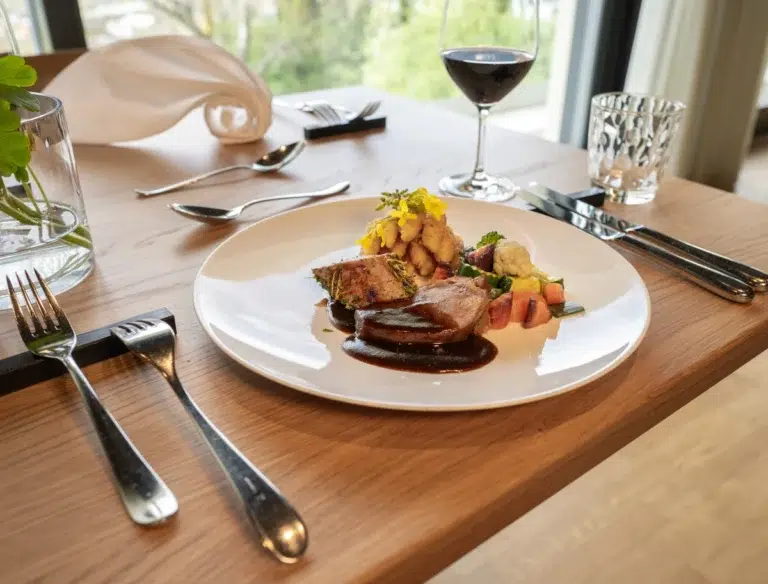 Ein Gourmet-Hoteldiät-Menü mit Wein an einem Holztisch, der für eine Person in der Nähe eines Fensters gedeckt ist.