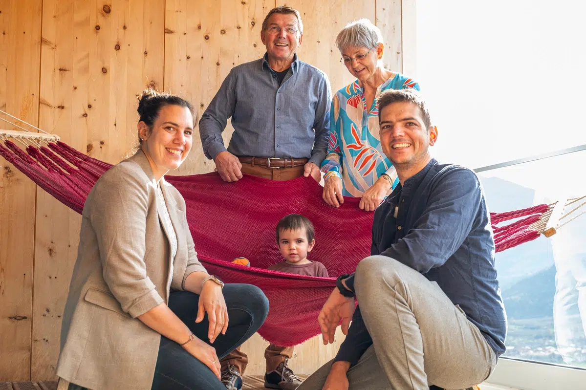Drei Erwachsene, zwei Senioren und ein Kind lächeln in einer Hängematte im Biohotel Südtirol am Fenster.