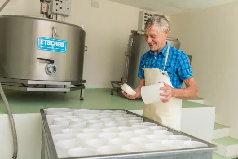 Lächelnder Mann in Schürze, wie Karl Thöni Mals, beim Hantieren mit Käseformen in einer Molkerei.
