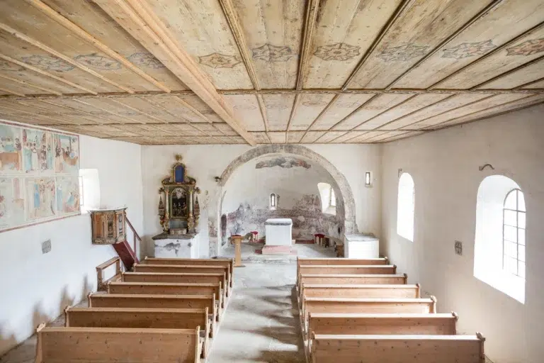 Kleines, rustikales Kircheninnere mit Holzbänken, Altar, Fresken und Bogenfenstern.
