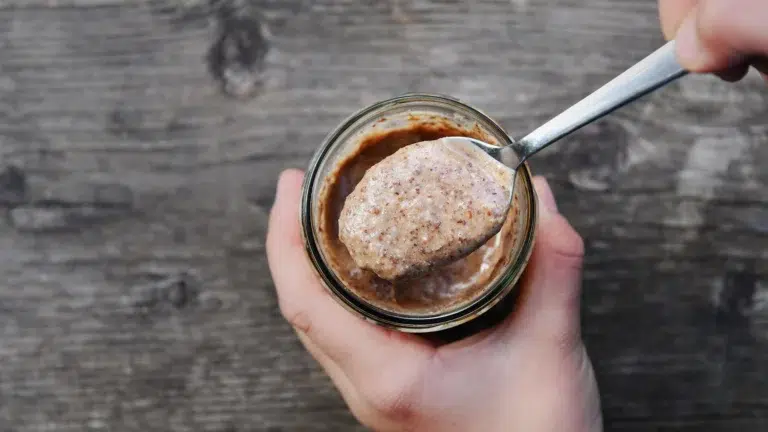 Eine Hand hält ein Glas mit Nussbutter, darüber hebt Daniel Primisser einen Löffel.