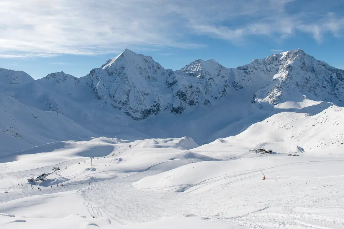 Schneebedeckte Berge und Skipisten unter einem blauen Himmel mit vereinzelten Wolken.