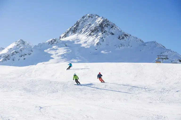 Drei Skifahrer fahren bei strahlend blauem Himmel einen verschneiten Berghang hinunter.