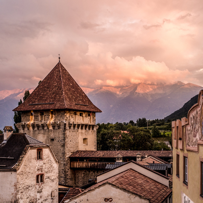 Ein mittelalterlicher Steinturm mit Ziegeldach bei Sonnenuntergang, im Hintergrund die Berge.