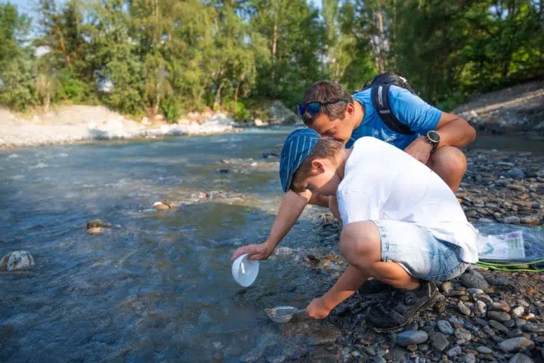 Adulto e bambino raccolgono campioni d'acqua sulla riva di un fiume in una giornata di sole.