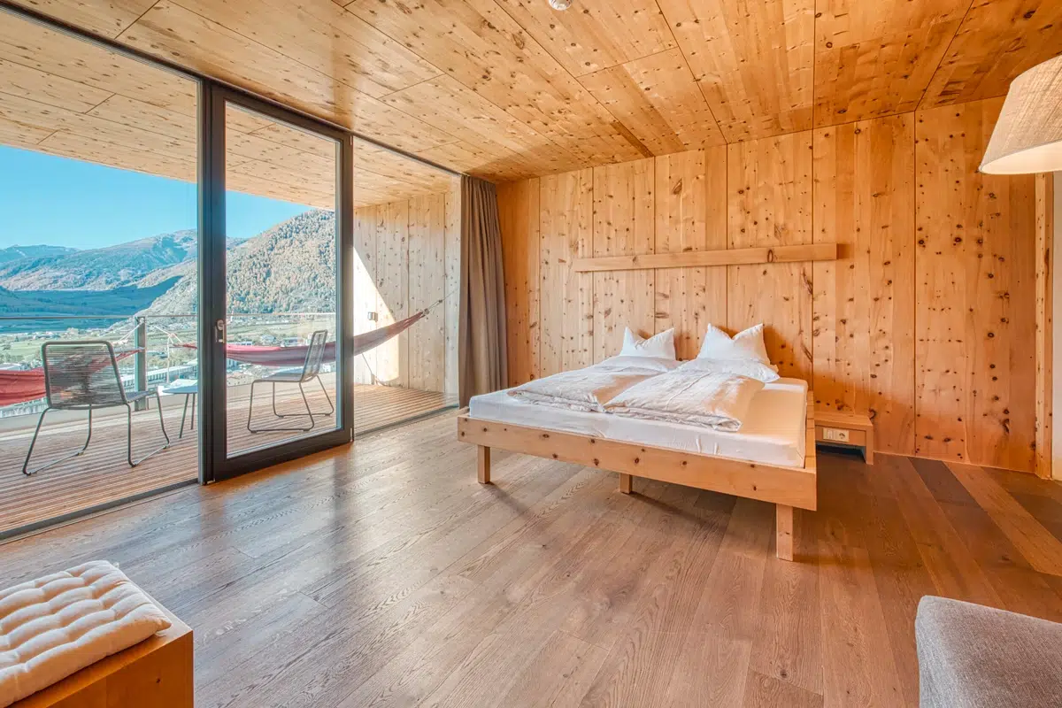 Wood-paneled bedroom with double bed, patio, hammock, and mountain view through glass doors.
